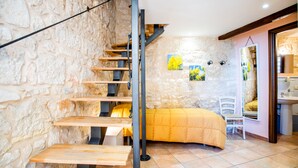 A bedroom with a stone wall, a bed with a yellow duvet, a wooden staircase, and a window with artwork. - Borgo Monachella (Ragusa)