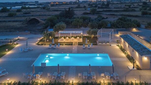 A rectangular swimming pool with lounge chairs and umbrellas, surrounded by a stone wall and vegetation. - Borgo Monachella (Ragusa)
