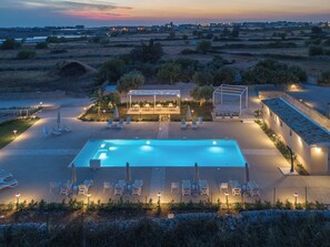 A rectangular swimming pool with lounge chairs and umbrellas, surrounded by a stone wall and vegetation.