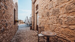 A narrow cobblestone street with stone buildings on either side, a round table with chairs, and outdoor seating. - Borgo Monachella (Ragusa)