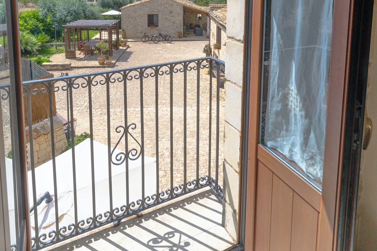 A balcony with a view of a stone building and a garden.