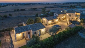 A stone house complex with multiple buildings, outdoor seating, and a well-lit patio area. - Borgo Monachella (Ragusa)
