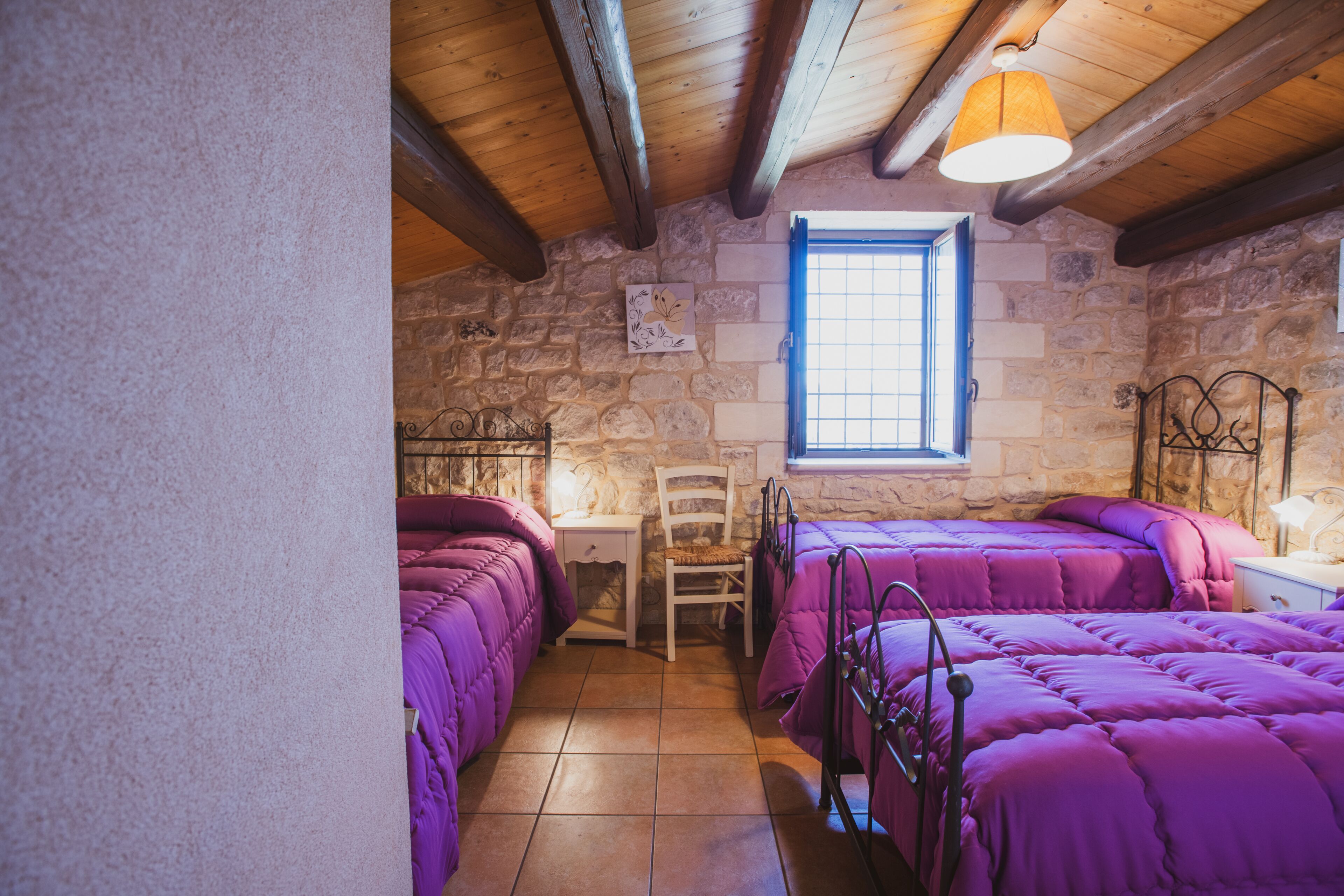 Una habitación con dos camas, una silla, una mesita y una ventana.