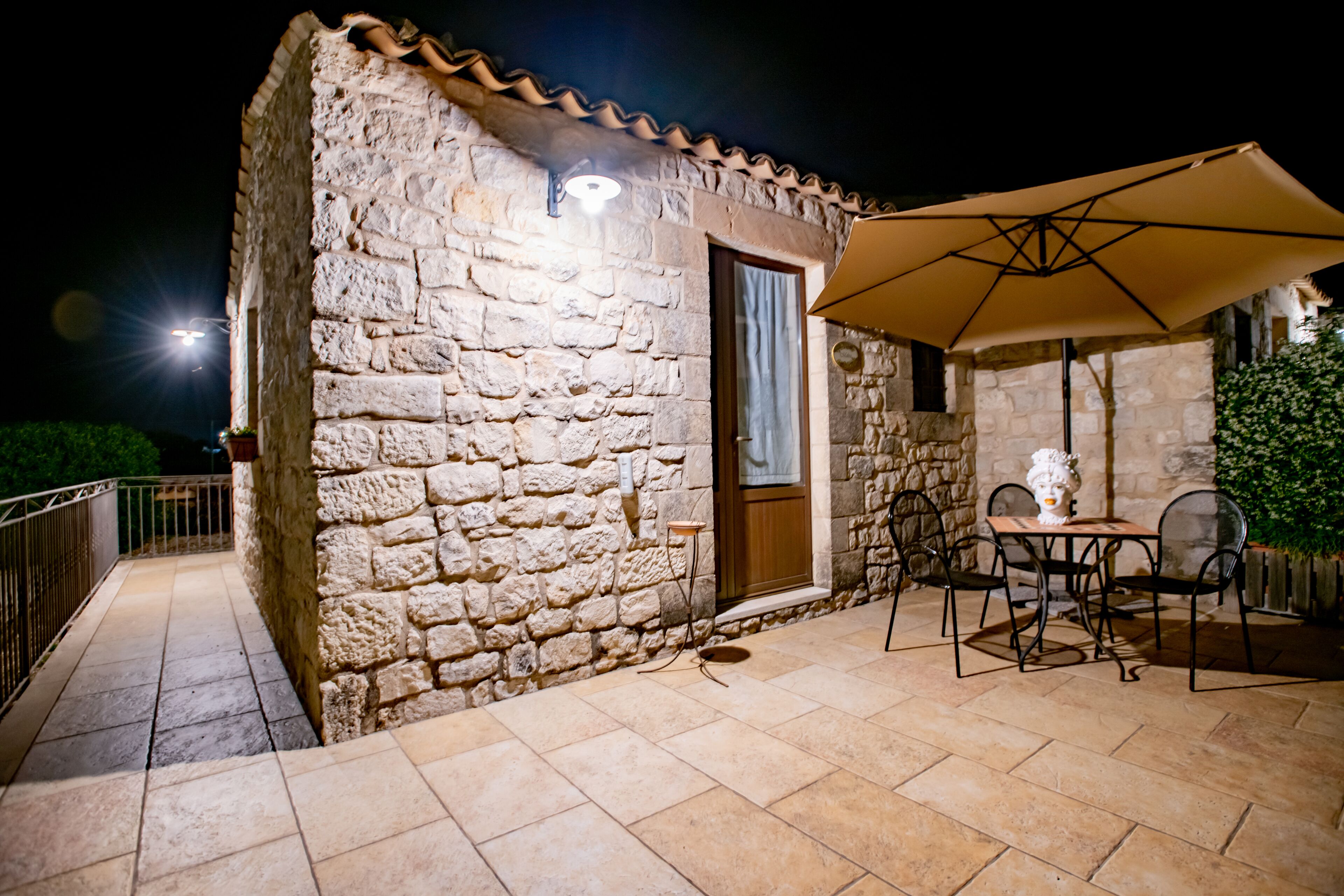 Un edificio de piedra con un patio empedrado, una mesa con sillas y una sombrilla.