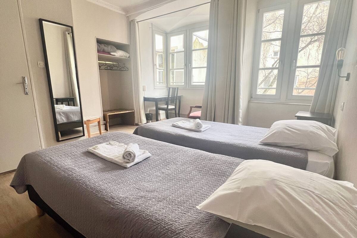 A hotel room with two beds, a desk, a chair, a wardrobe, and a window with curtains.