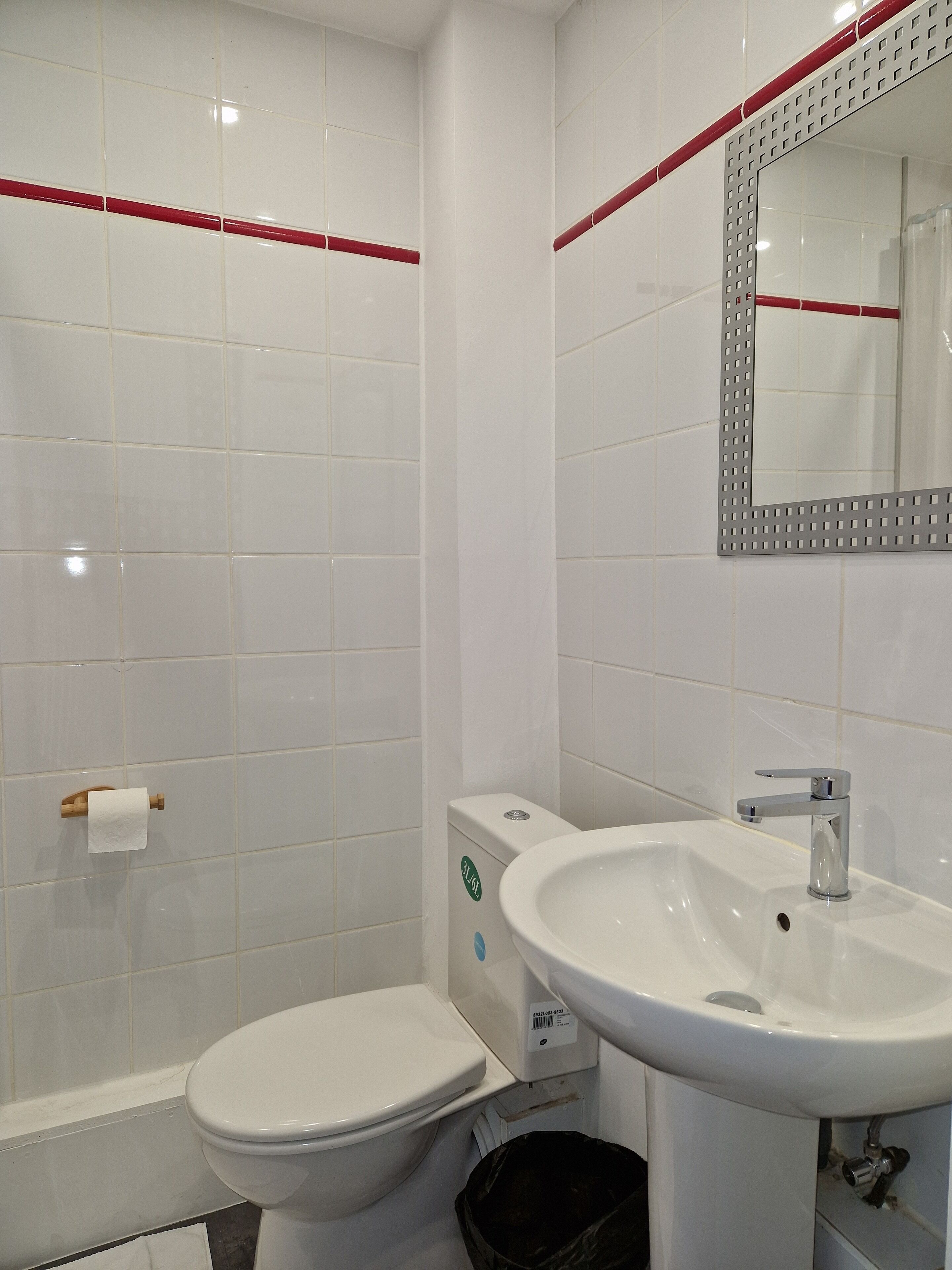 Een badkamer met witte tegels, een toilet, een wastafel en een spiegel.