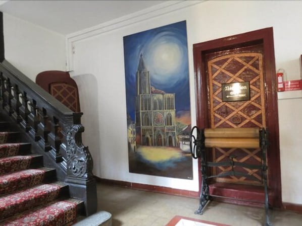 Una escalera con barandillas ornamentadas, un mural de una catedral y una puerta con un letrero que dice 'Hotel'.