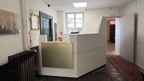 A reception area with a counter, a radiator, a fire extinguisher, and a window with blinds. - Hotel Patricia (Strasbourg)