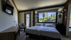 A bedroom with two beds, a desk, and a chair. There are windows with views of greenery outside. - Hotel El Varadero (Tarifa)
