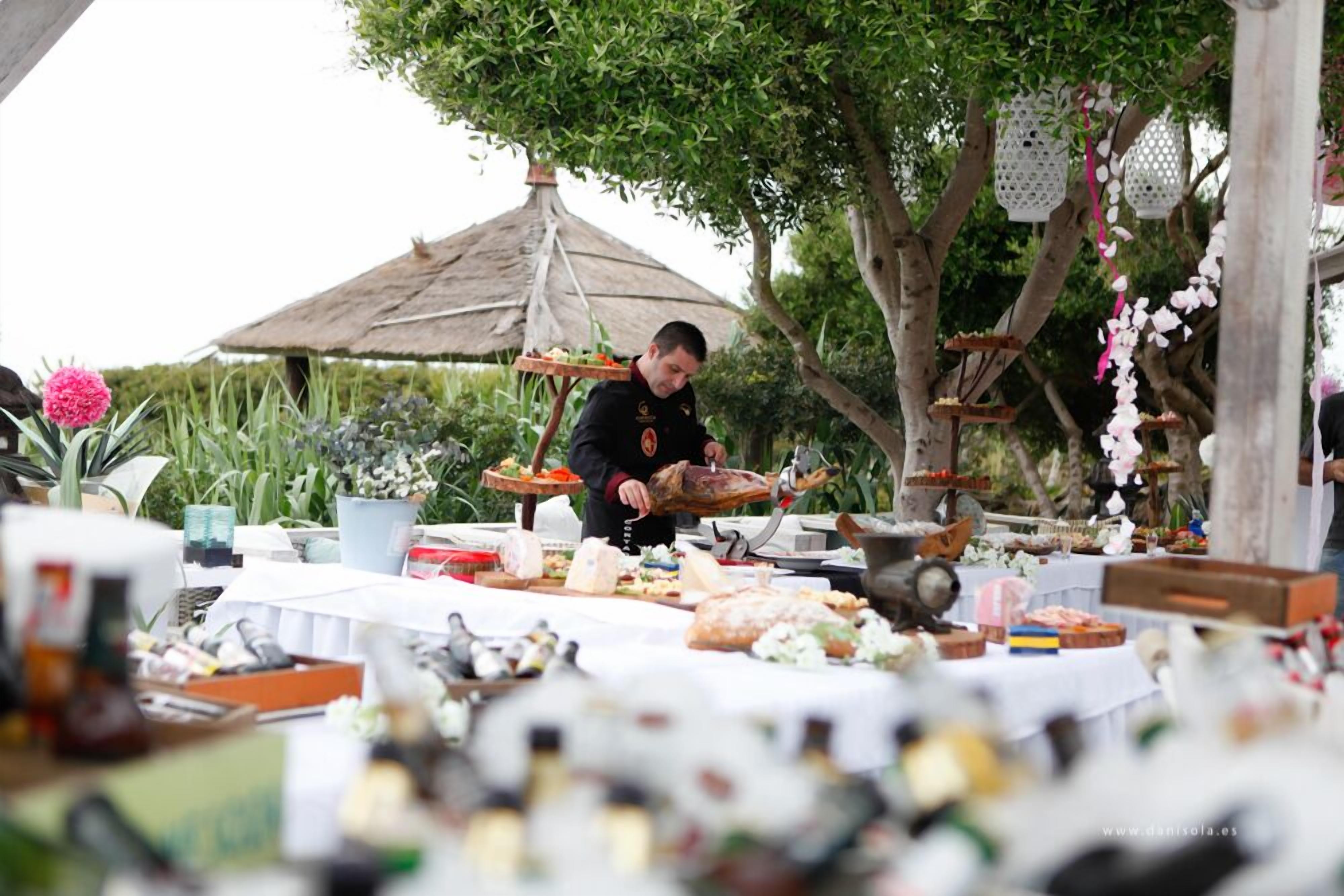 Evento al aire libre con un chef preparando comida, rodeado de diversos alimentos y decoraciones.