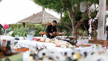 Evento al aire libre con un chef preparando comida, rodeado de diversos alimentos y decoraciones.