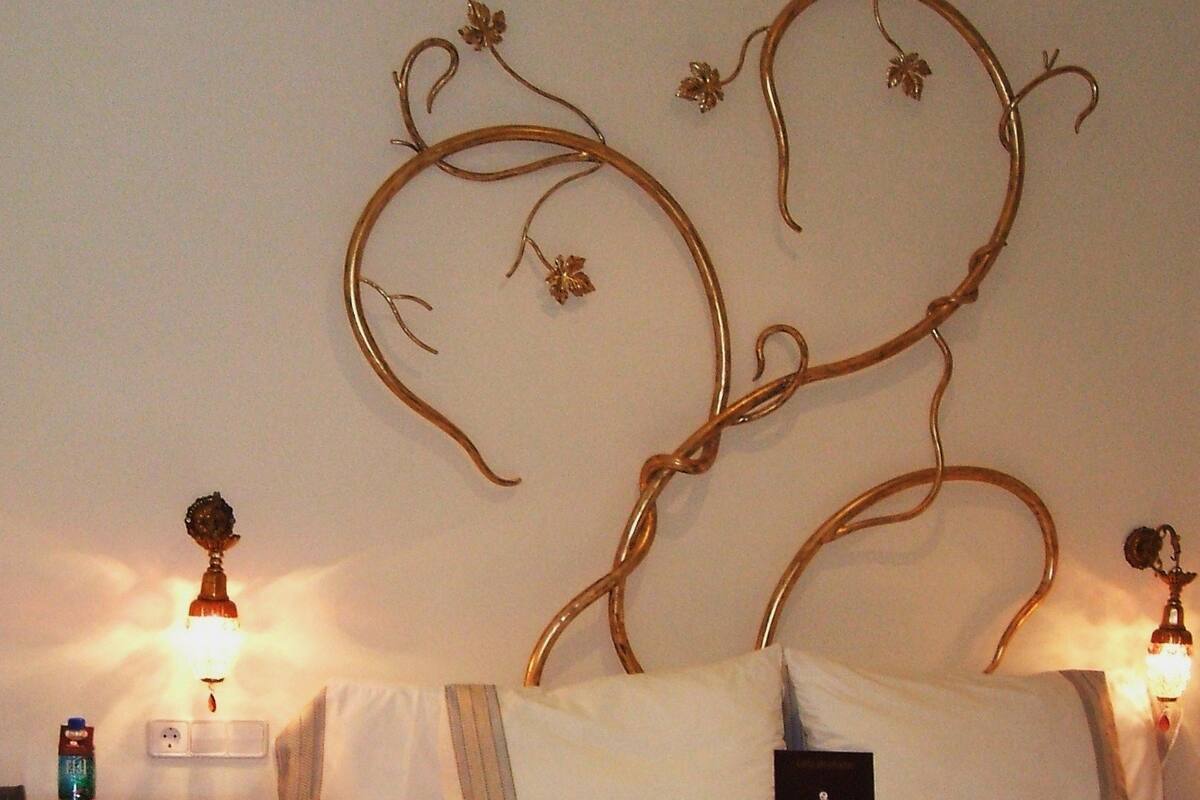 A neatly made bed with white linens and two folded towels, a wooden headboard with floral designs, and bedside lamps on either side.