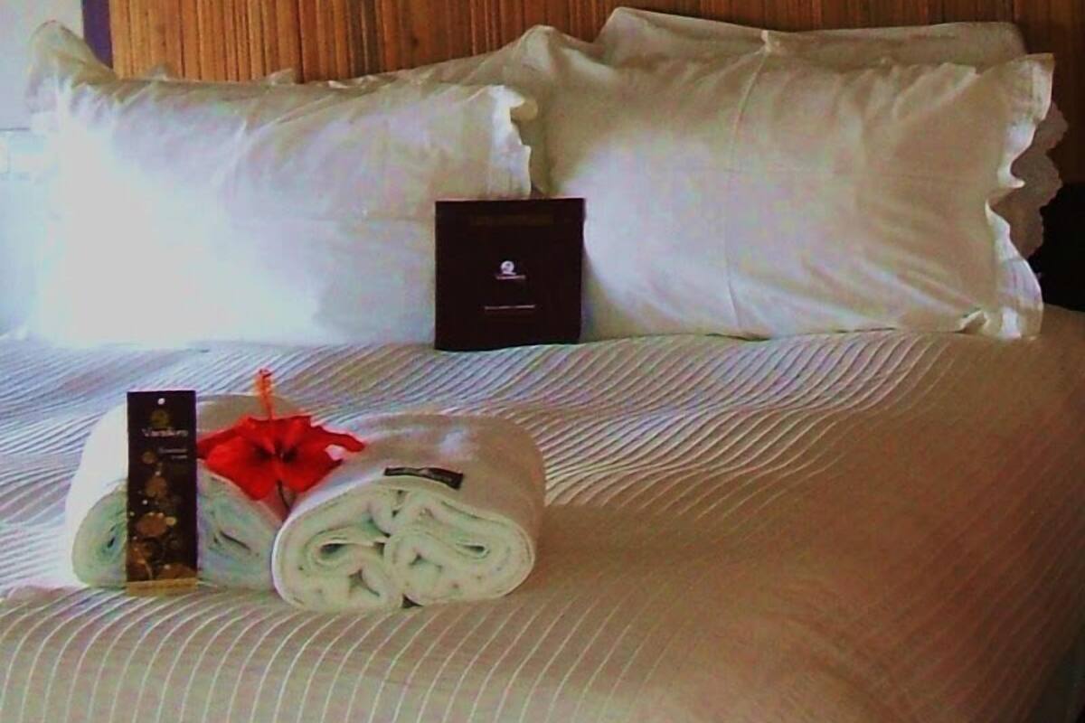 A neatly made bed with rolled towels and a small box, likely containing toiletries, on a hotel room bed with striped bedding.