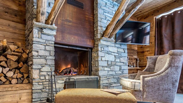 Una habitación acogedora con chimenea de piedra, un televisor montado en la pared y un sillón cómodo.