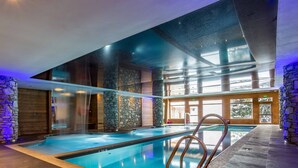 Una piscina interior con pilares de piedra, techo de cristal y vistas al exterior.