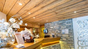 Un mostrador de recepción de madera con un fondo de pared de piedra, un televisor y una pieza decorativa de metal.