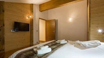 A wooden-paneled room with a bed, towels, a television, and a door.
