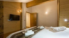 Une pièce aux murs lambrés, équipée d’un lit, de serviettes, d’un téléviseur et d’une porte.