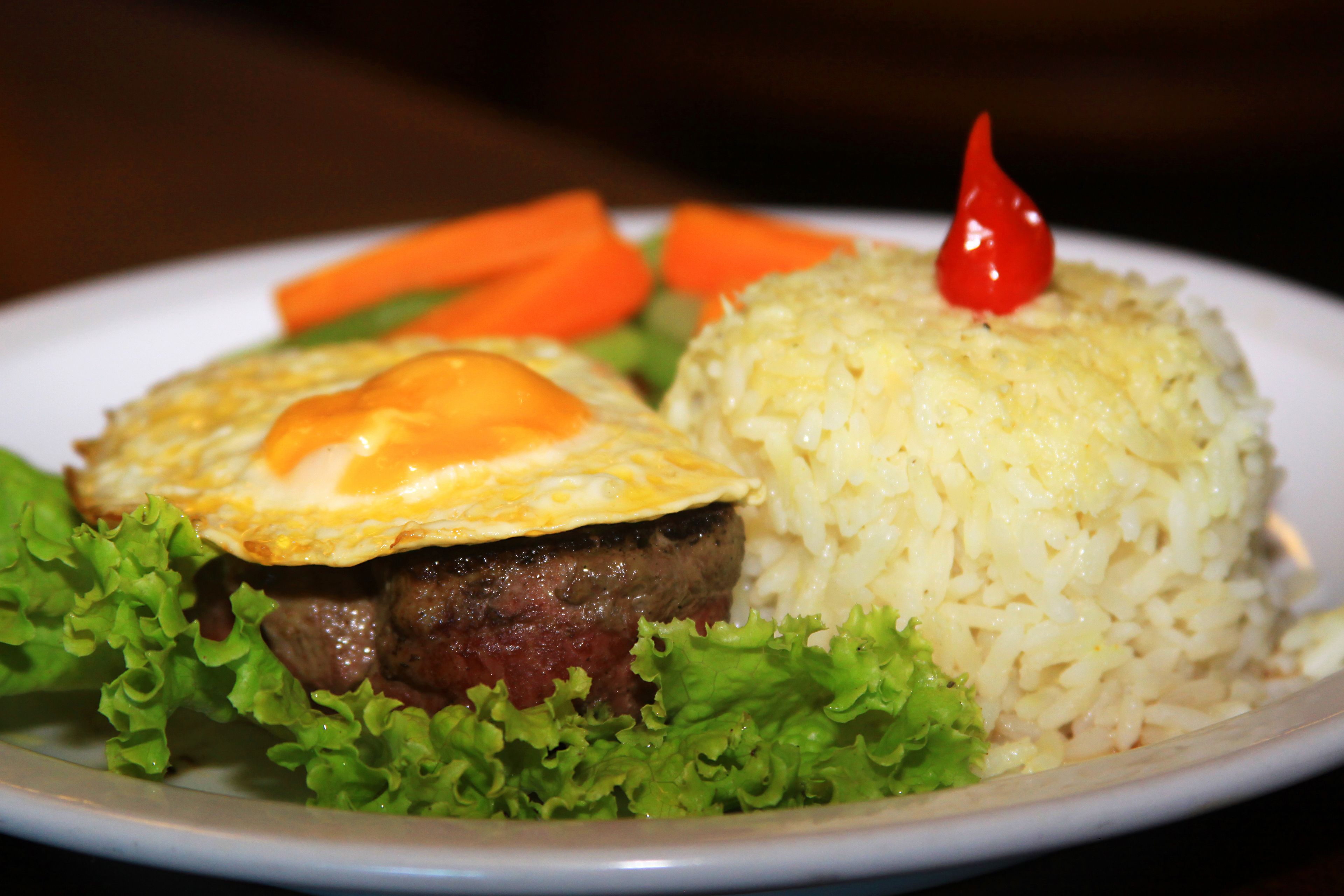 A plate with a hamburger, fried egg, rice, and vegetables.