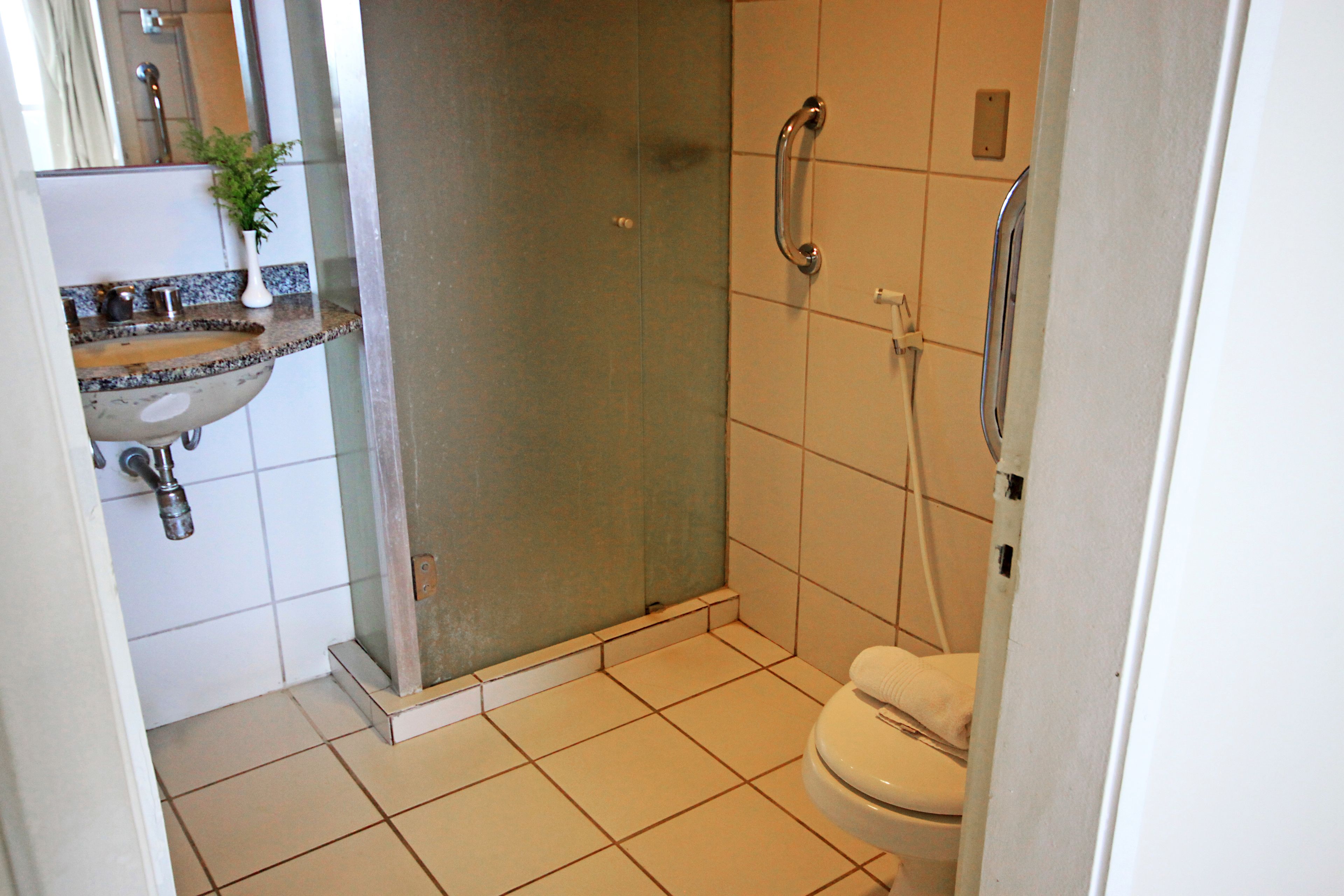 A bathroom with a shower, toilet, sink, and a small plant.