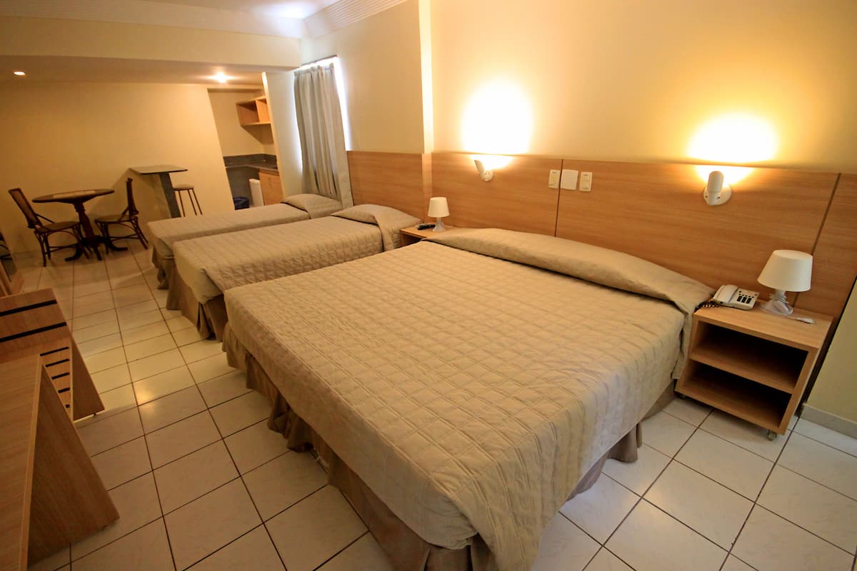 A hotel room with two beds, a desk, a chair, and a small kitchenette.