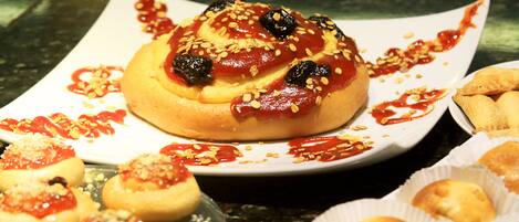 A table with various pastries, including a large bun topped with sesame seeds and a sauce, and smaller buns in paper cups.