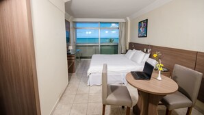 A hotel room with a bed, a desk with a laptop, a chair, and a view of the ocean. - Jangadeiro Hotel e Convenções (Recife)