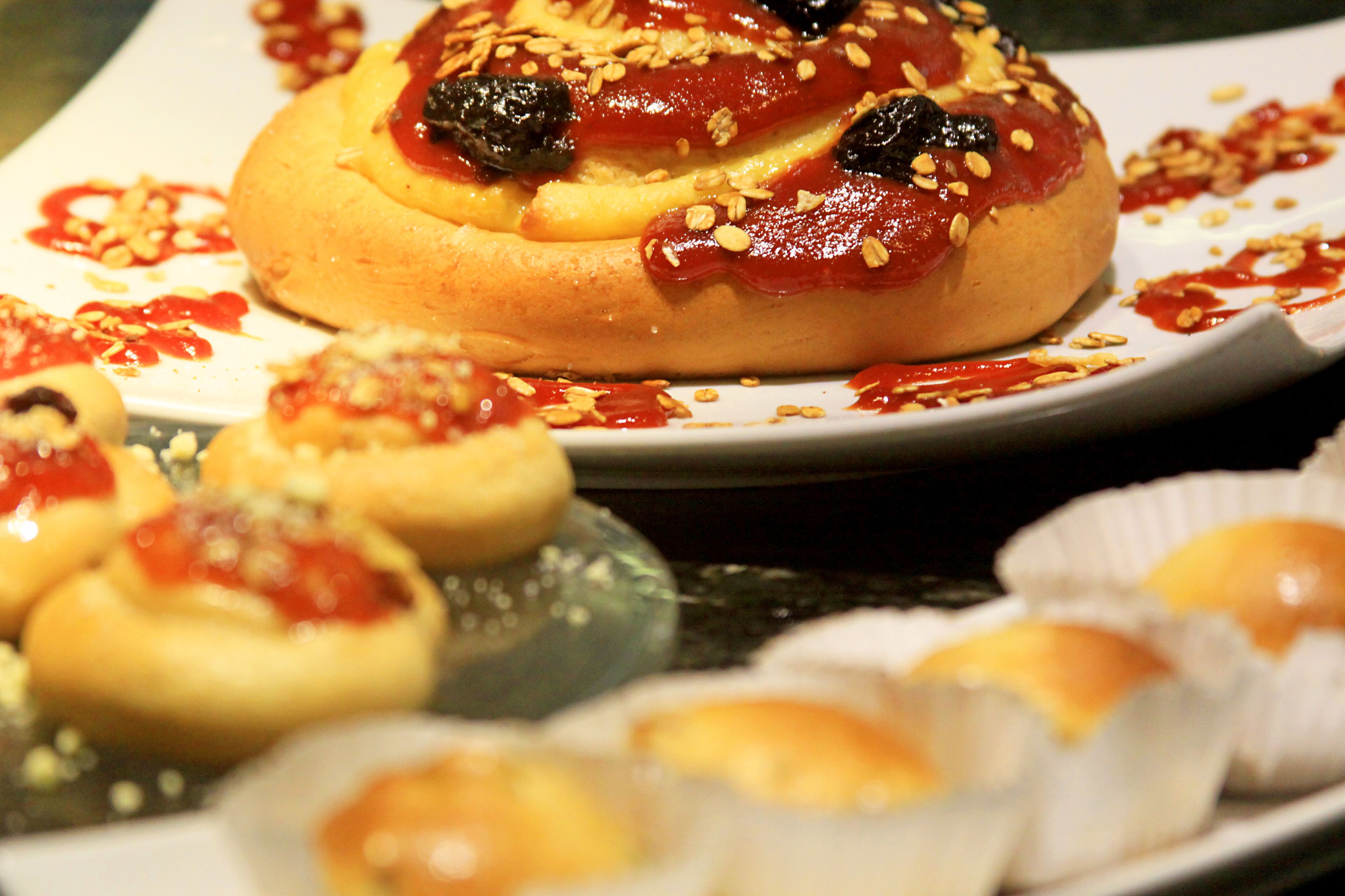 A variety of pastries on a plate, including a large bun with toppings and smaller buns in paper cups.