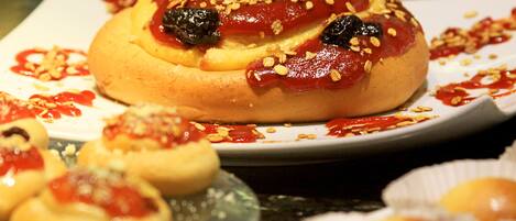A variety of pastries on a plate, including a large bun with toppings and smaller buns in paper cups.