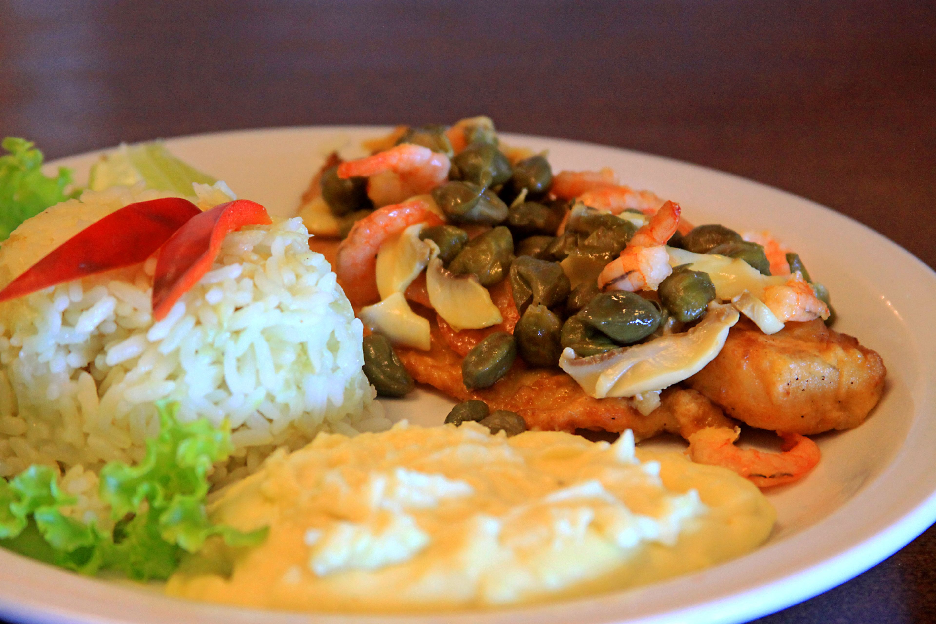 Un plato de comida con arroz, camarones, alcaparras y un acompañamiento cremoso.
