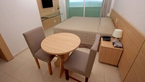 A hotel room with a bed, a bedside table with a lamp, a TV on the wall, and a view of the sea. - Jangadeiro Hotel e Convenções (Recife)