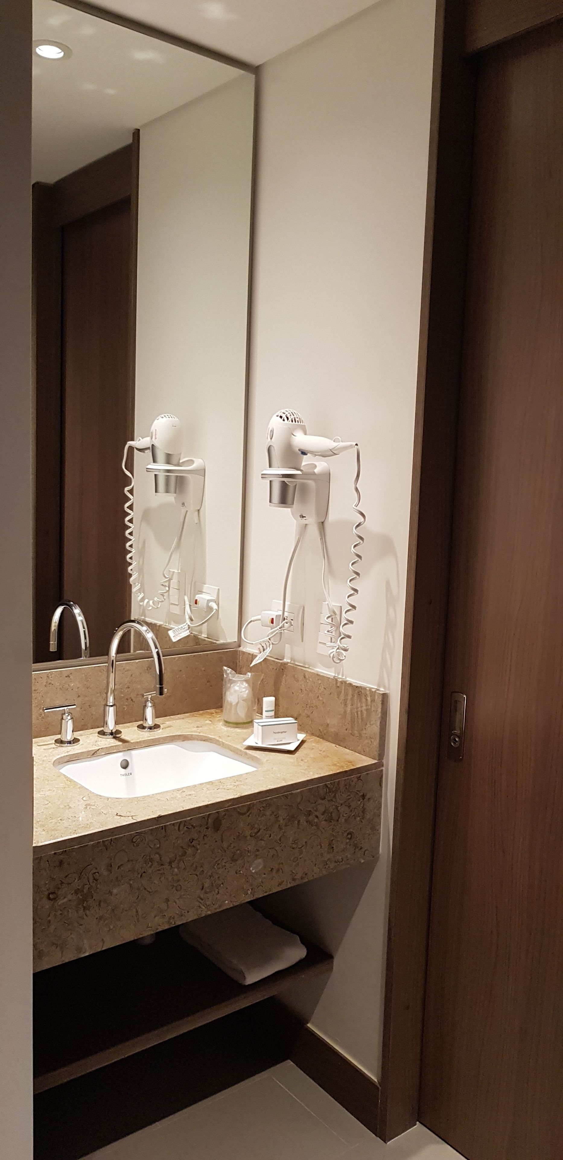 A bathroom with a large mirror, a sink, and two hair dryers mounted on the wall.