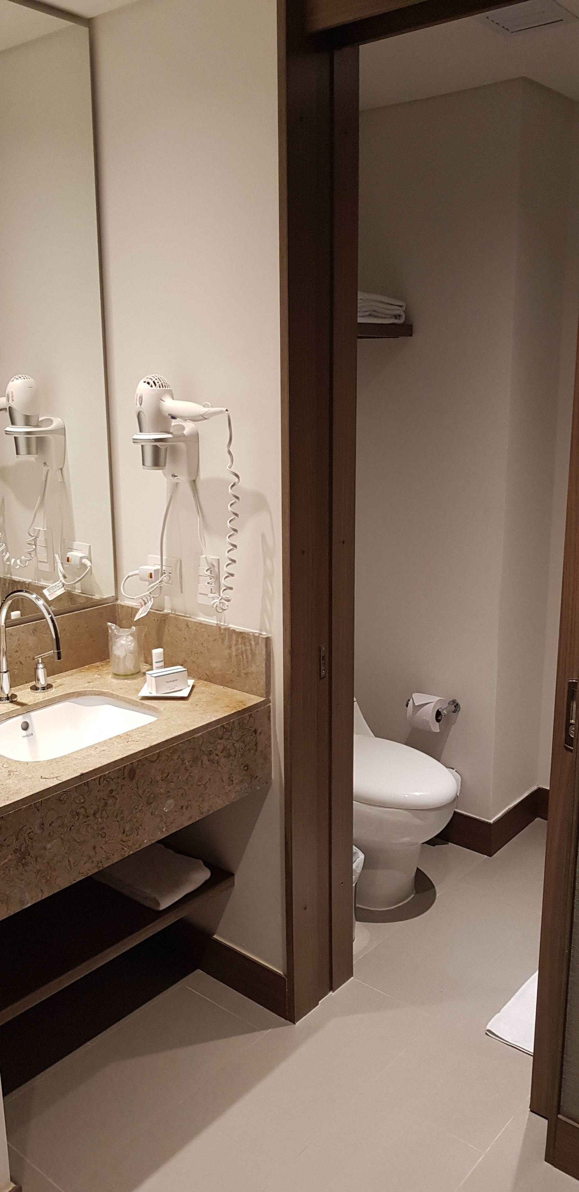 A bathroom with a sink, mirror, hairdryer, and toilet.