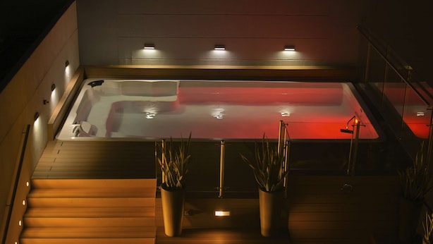 Un área de spa moderna con suelo calefaccionado, una bañera roja climatizada y plantas en macetas.
