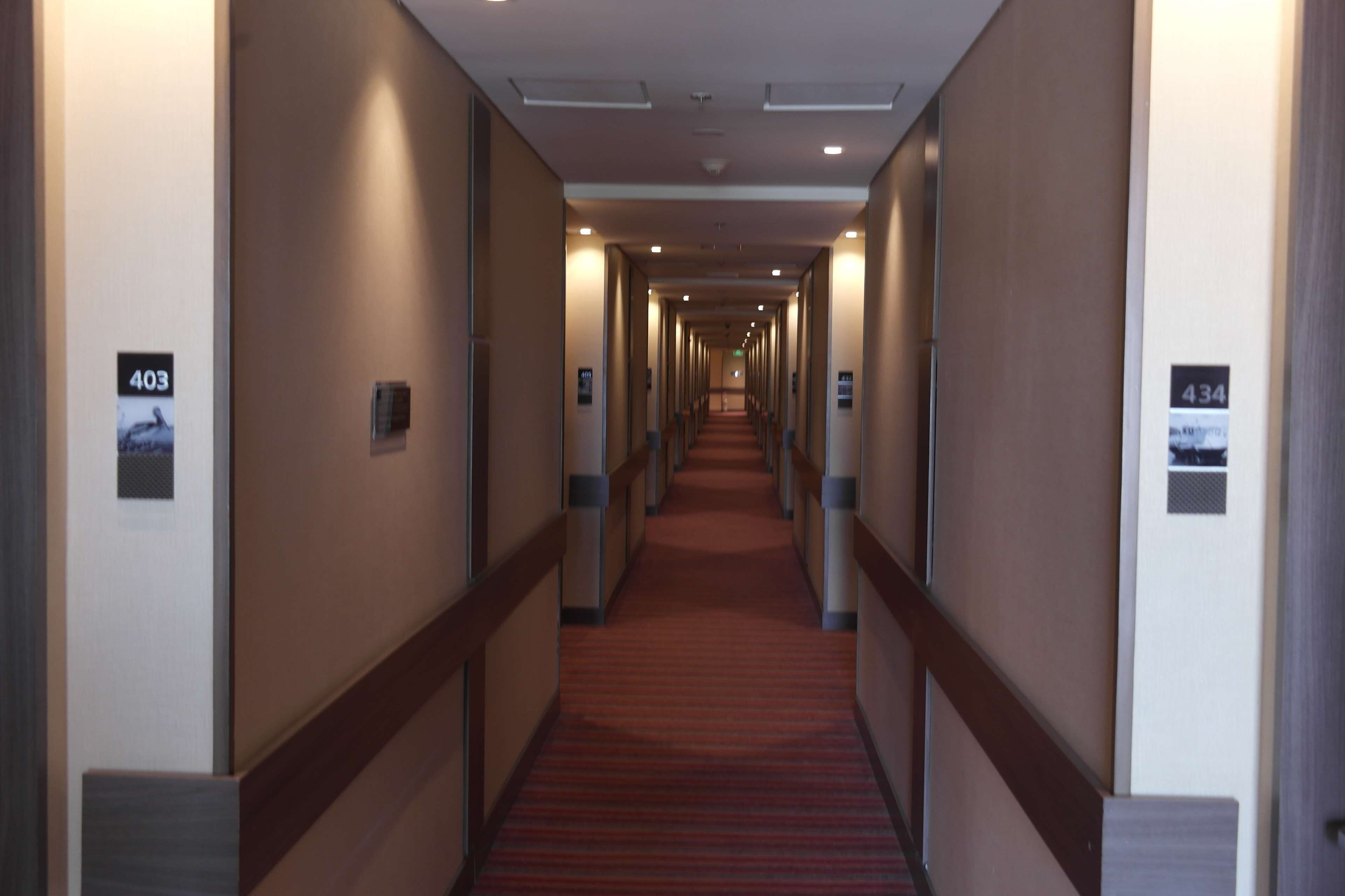 Een hotelgang met een rood tapijt, genummerde deuren en een modern design.