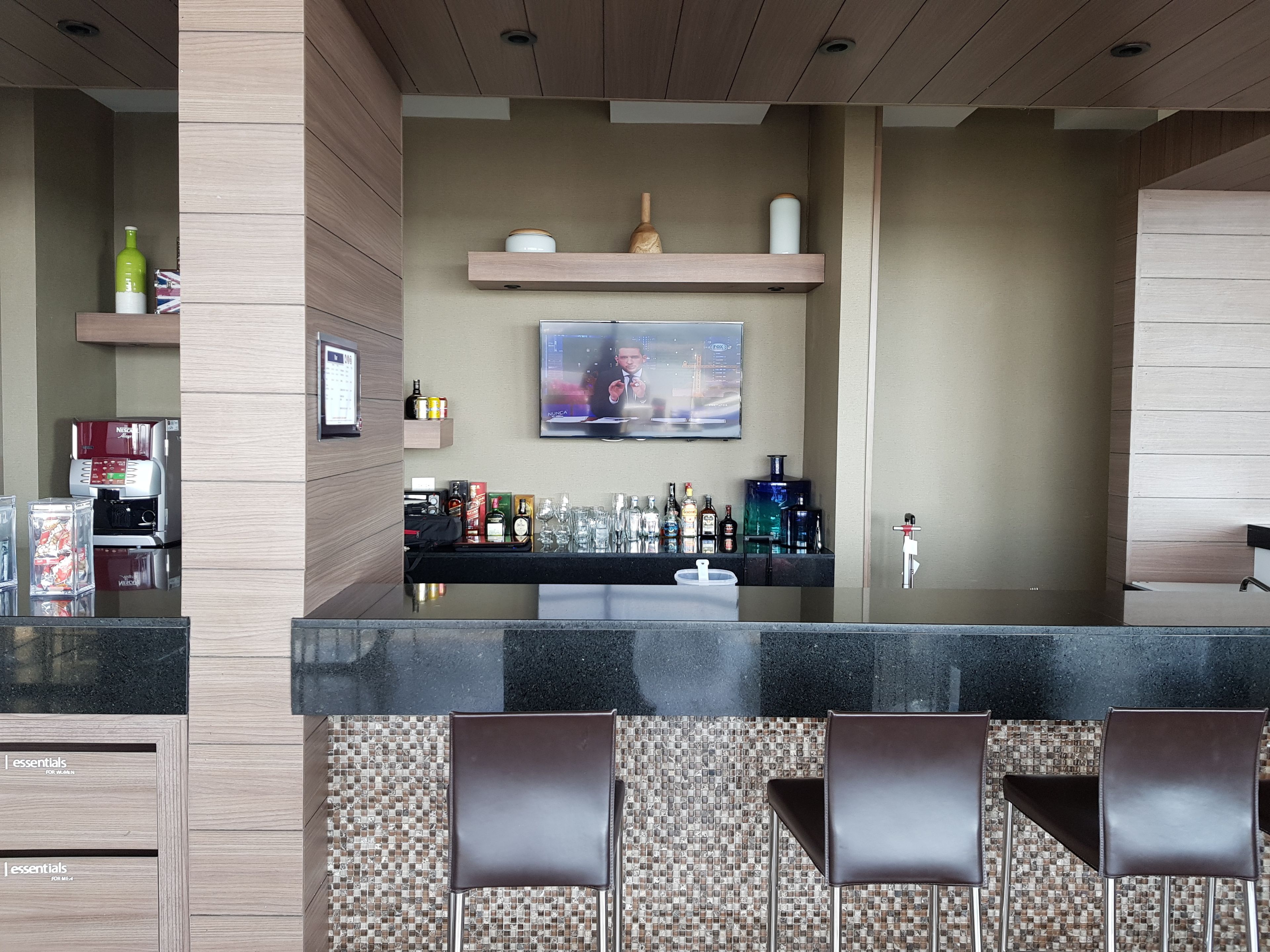 Een moderne barruimte met een flatscreen televisie, barstoelen en een verscheidenheid aan drankflessen.