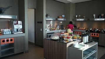 A modern kitchen area with a coffee machine, various food stations, and a person preparing food.