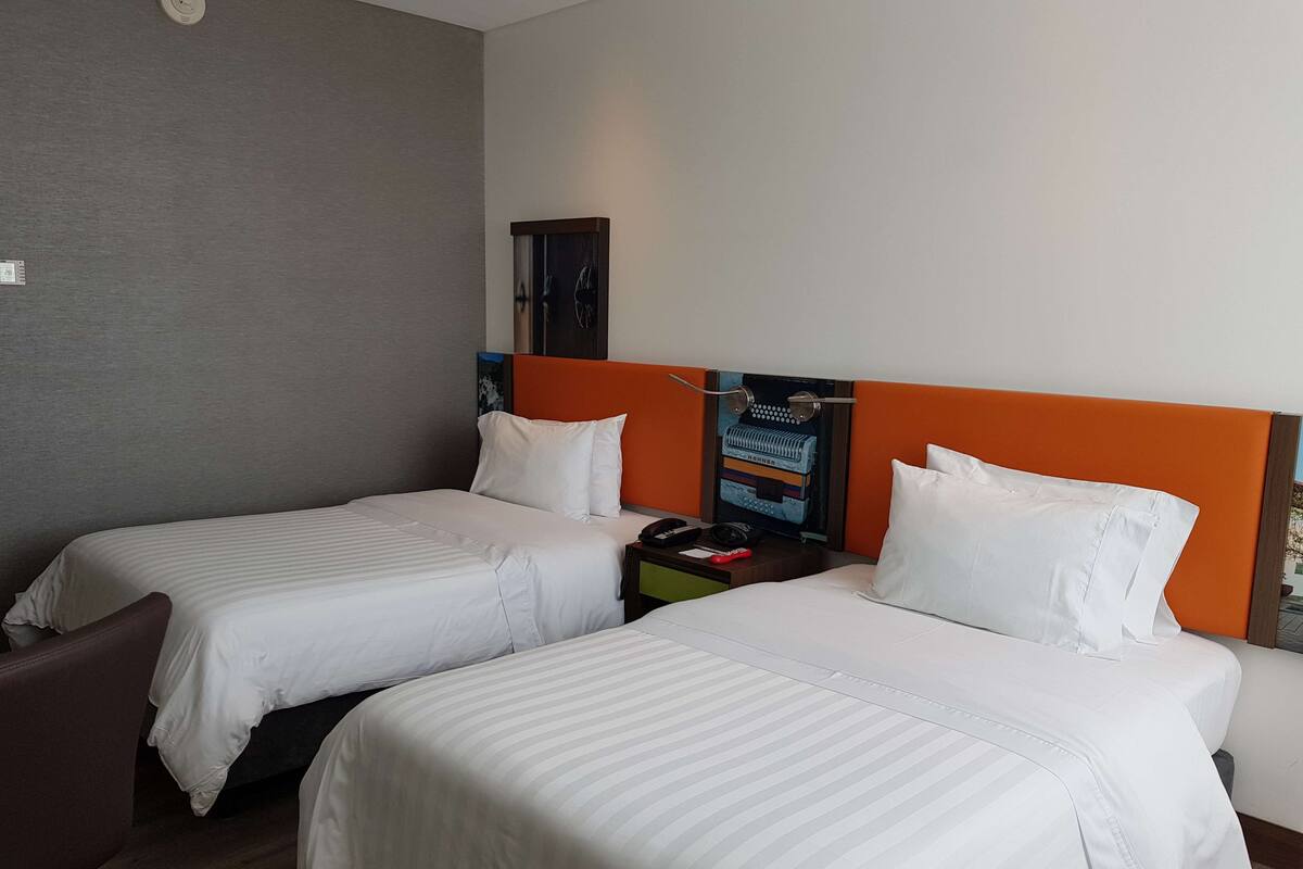A hotel room with two single beds, a nightstand, a telephone, and a wall-mounted clock.