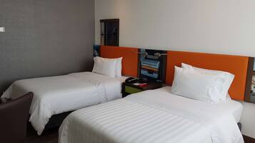 A hotel room with two single beds, a nightstand, a telephone, and a wall-mounted clock.