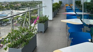 Una terraza moderna al aire libre con mesas y sillas azules y amarillas, plantas en macetas y vistas a la ciudad y las montañas al fondo.