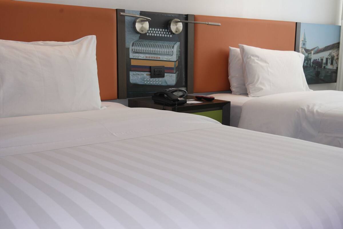 Una habitación de hotel con dos camas, una mesita de noche con teléfono y un reloj en la pared.