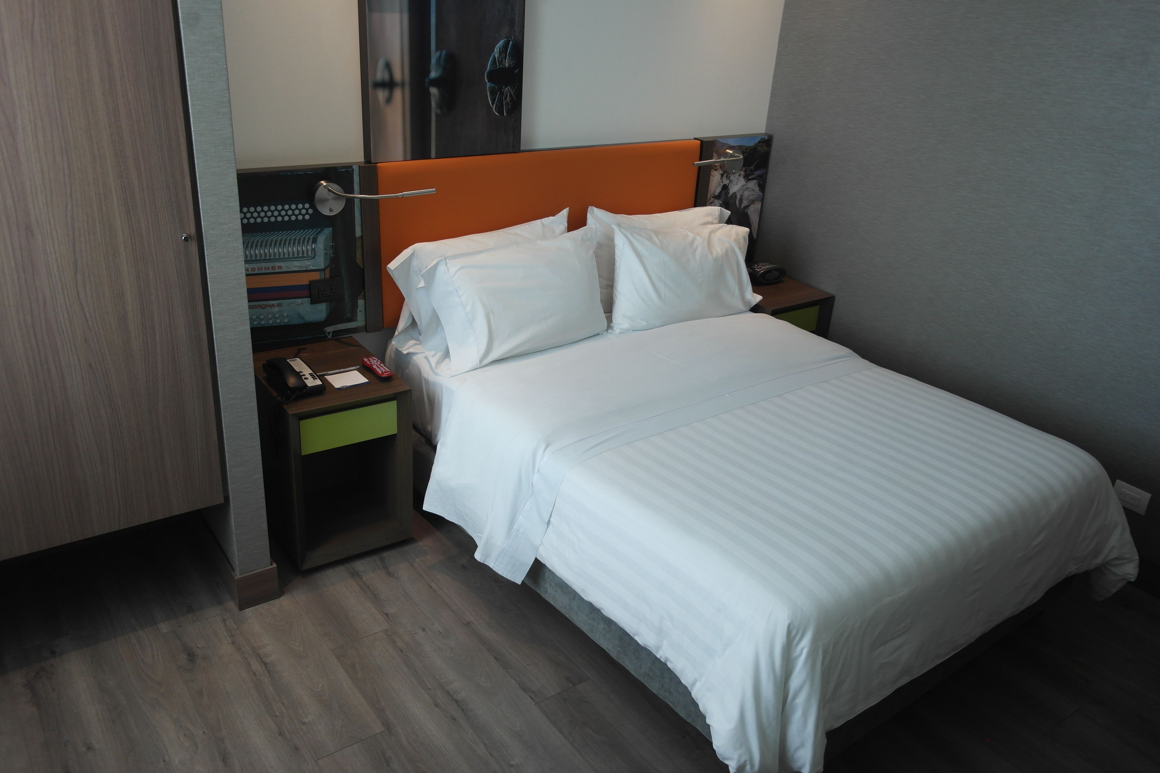 A hotel room with a bed, a nightstand, a desk with a lamp, and a wardrobe.