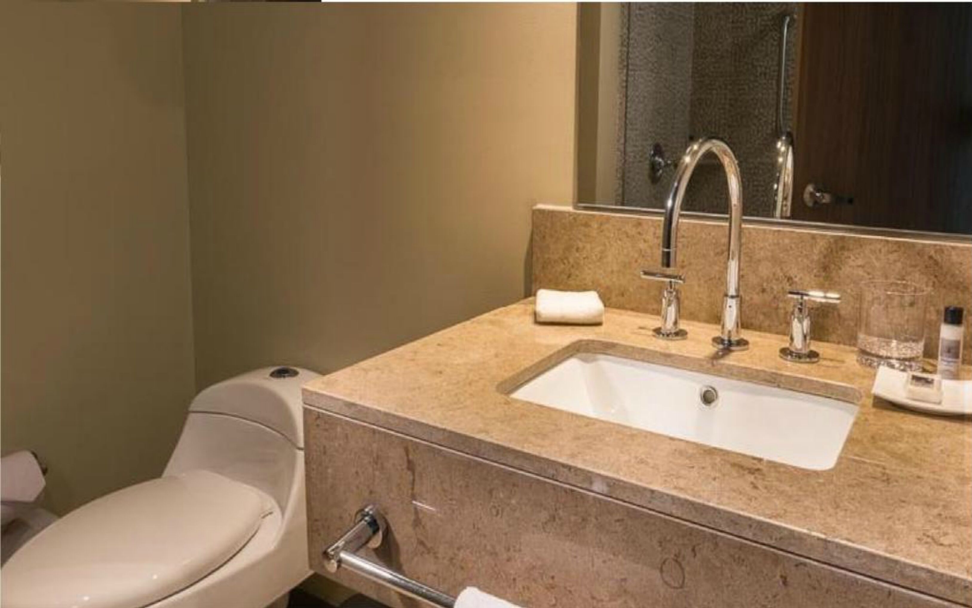 A bathroom with a white toilet, a beige sink with a mirror above it, and a towel on the counter.