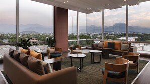 Un salón moderno con ventanas amplias, asientos cómodos y vistas a montañas y al paisaje urbano.