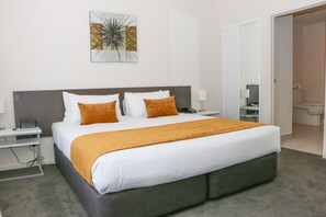 A modern hotel room with a large bed, a bedside table, a nightstand, a wall-mounted artwork, and a bathroom visible through an open door.