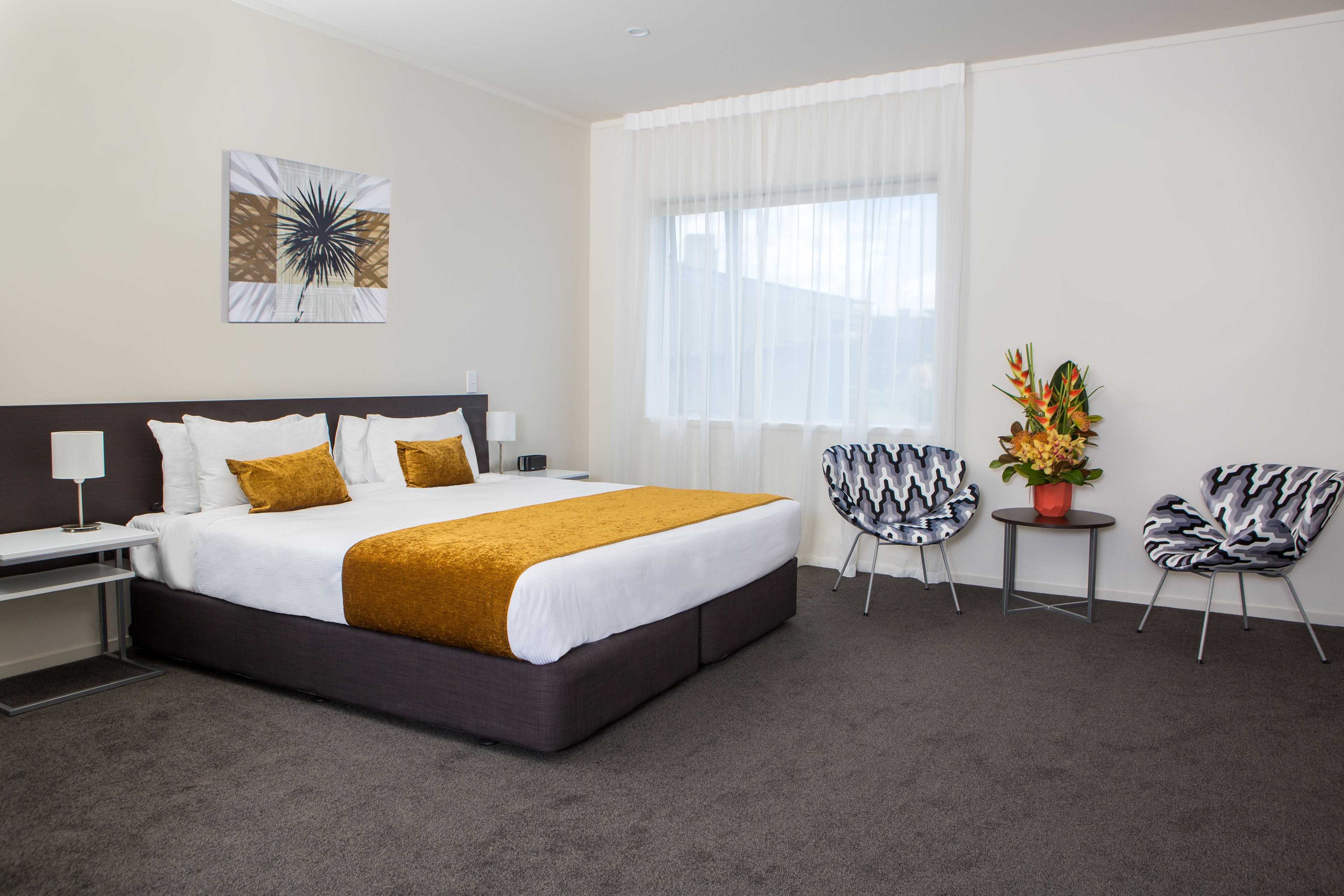 Een moderne hotelkamer met een groot bed, een bureau, twee stoelen en een raam met dunne gordijnen.