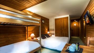 Una habitación tipo cabaña de madera con dos camas individuales, una mesita con una taza y un televisor en la pared.