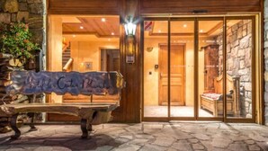 A stone-floored entrance to a hotel with a wooden bench and a sign. - Les Crêtes Blanches (Val-d'Isere)
