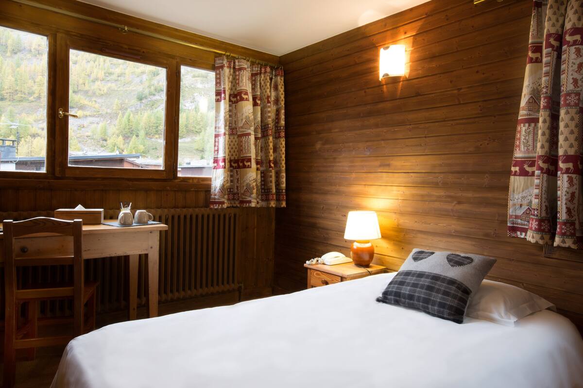 A wooden cabin room with a bed, a desk, and a chair.