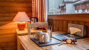 A wooden interior with a table, a lamp, a window with a view of traditional buildings, and a tissue box. - Les Crêtes Blanches (Val-d'Isere)